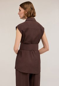 Top marrone con cintura, dalla finitura testurizzata, maniche corte e colletto a risvolto, caratterizzato da un orlo arrotondato e una vestibilità ampia.