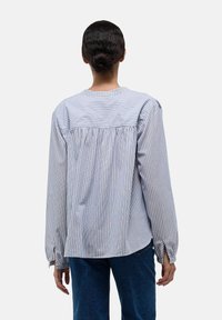 Chemise à rayures à manches longues en bleu clair et blanc, avec un dos froncé, un col rond et des poignets boutonnés. Texture de tissu douce.