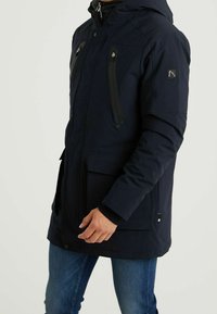 Granatowa, wodoodporna kurtka z kapturem, wyposażona w dwie zapinane na zamek kieszenie na piersi, kieszenie z przodu oraz teksturowane akcenty materiałowe.