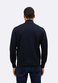 Maglione blu navy a maglia con colletto e polsini a costine, caratterizzato da una texture liscia e un design aderente, abbinato a jeans in denim scuro.