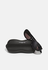 Black sunglasses with oval frames, dark lenses, and logo detailing. Accompanied by a rounded black case with a zipper and white logo.