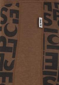 Brauner Stoff mit einem wiederholenden schwarzen Textmuster. Das Material ist gerippt mit einer sichtbaren Naht und einem kleinen weißen Etikett mit dem "SLOPE"-Logo.