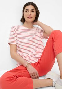 Gestreept T-shirt met rode en witte horizontale lijnen, gecombineerd met koraalkleurige broeken. Accessoires omvatten gouden armbanden. Casual, slanke pasvorm.