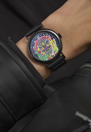 Timex polshorloge met een zwart lederen band, met een kleurrijk schedelontwerp op een donkere wijzerplaat, geaccentueerd met bloemmotieven en witte uurmarkeringen.