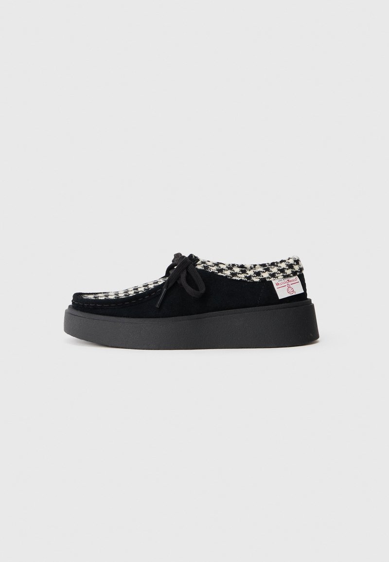Chaussure à plateforme en daim noir avec un col en tissu pied-de-poule noir et blanc, lacets noirs et une étiquette de marque blanche sur le col du talon.