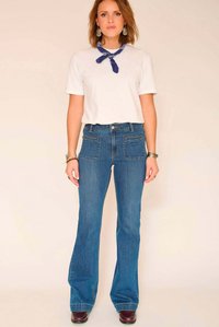 Jean bleu évasé avec une taille mi-haute et deux poches avant, associé à un t-shirt blanc et un bandana bleu autour du cou.