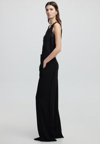 Top negro transparente sin mangas con detalles de encaje, combinado con pantalones negros de pierna ancha de cintura alta, que cuentan con bolsillos laterales y una textura suave.