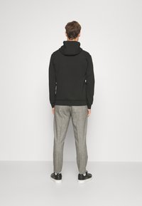 Svart hoodie med känguruficka och dragsko i huvan, ihop med grå strukturerade byxor och svarta sneakers.