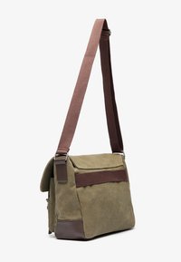 Olive green messenger bag with a brown fabric strap, a front flap, and a dark brown accent at the base. Features a zippered pocket on the side.