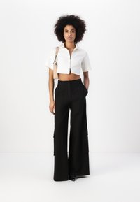 Camisa blanca corta con cremallera y mangas cortas, combinada con pantalones de talle alto, negros y de pierna ancha, con bolsillos laterales. Texturas suaves, diseño minimalista.