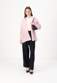 Lys rosa, luftig cardigan med åpen front, båret over en hvit skjorte. Svarte vide bukser med stripete mønster og svarte hæler.