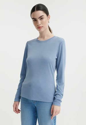 Langärmliges, hellblaues Oberteil aus einem strukturierten Stoff. Mit rundem Halsausschnitt und taillierter Passform. Getragen mit Jeans.