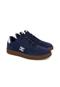 Pair of navy blue DC sneakers with brown soles, white logo on sides, and white heel accents, shown against a white background.