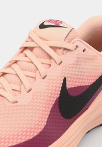 Nike shoe featuring a textured light pink upper, dark pink accents, black swoosh logo, and flat beige laces, with a smooth, modern design.
