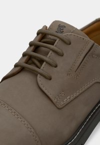 Ανοιχτό καφέ δερμάτινο παπούτσι με στρογγυλή μύτη, πέντε ελαιόχρωμα κορδόνια, διακοσμητική ραφή και ένα μικρό λογότυπο στο πλάι.