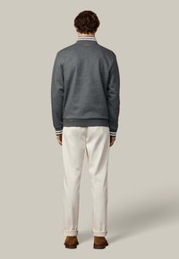 Grijze sweatshirt met een geribbelde kraag en gestreepte accenten, gecombineerd met crèmekleurige broeken. Model zichtbaar van achteren. Bruine schoenen zichtbaar.