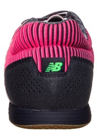 Sportskor med överdel av rosa ribbad tyg, svart mockahäl, grön logotyp och gummisula med mönstrad yta.