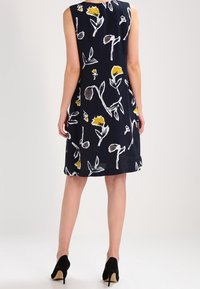 Bezramenné námořnické šaty s květinovým vzorem v žluté a hnědé barvě, rovného střihu a jemné textury. Vybaveny černými lodičkami.