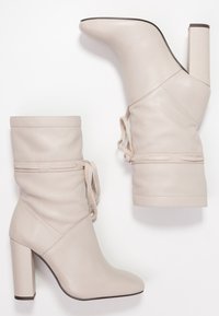 Bottines en cuir beige avec un talon bloc haut. Présentent un design froncé, une fermeture à lacets et une texture lisse.