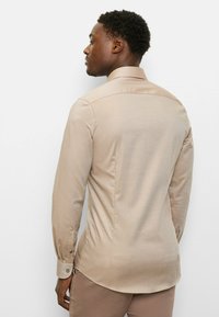 Hellbeiges Langarmshirt aus glattem Stoff mit subtiler Textur, ausgestattet mit einem klassischen Kragen und geknöpften Manschetten.