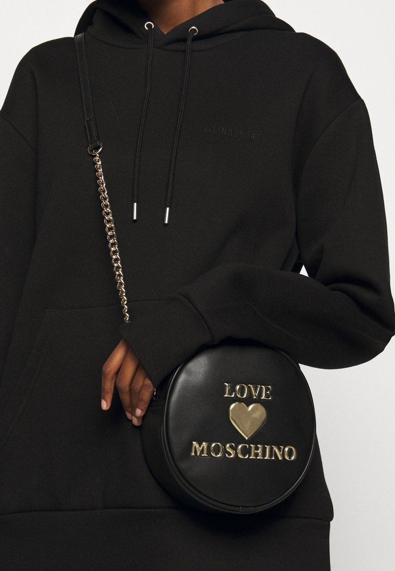 Borsa a tracolla rotonda nera in pelle con lettering dorato embossato "LOVE" e un cuore, dotata di una tracolla a catena dorata. Superficie testurizzata.