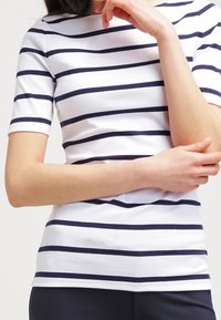 Kortärmad, figurnära topp med horisontella marinblå ränder på en vit bakgrund, tillverkad av ett mjukt, stretchigt tyg med rund halsringning.