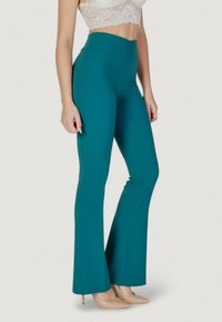 Pantaloni svasati color teal realizzati in un tessuto elastico, con vita alta e una texture liscia. Indossati con un crop top in pizzo e tacchi nudi.