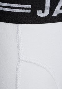 Fehér stretch anyagú boxer alsónemű fekete elasztikus derékkal, amelyen "J" felirat található, sima textúrával és látható varrási részletekkel.