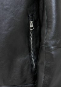 Schwarze Lederjacke mit seitlichem Reißverschluss, glatter Textur, subtiler Maserung und taillierten Nähten, die ein schlankes, eng anliegendes Design betonen.