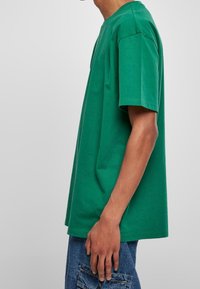 Zelené bavlněné tričko se volným střihem, krátkými rukávy a kulatým výstřihem. Viditelné švy podél švů. Nosit s modrými džíny.