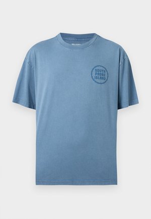T-shirt blu a maniche corte con scollo a girocollo, con la scritta "South Padre Island" all'interno di un motivo a catena circolare sul petto a sinistra.