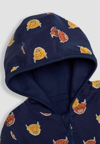 Felpa blu navy con cappuccio caratterizzata da un motivo di volti di animali illustrati in arancione, giallo e rosso. Texture morbida con chiusura a zip e cappuccio.