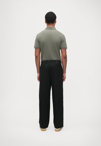 Polo vert olive, associé à un pantalon noir ample. Le polo comporte un col et des manches courtes, avec un pantalon à jambes droites.