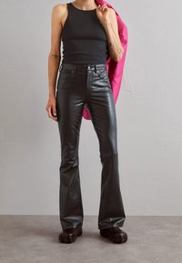 Czarne skórzane spodnie z szerokimi nogawkami o gładkiej fakturze, wysoki stan i przednie kieszenie. Połączone z dopasowaną czarną koszulką na ramiączkach i różową marynarką.