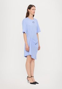 Light blue striped dress with short sleeves, featuring an asymmetrical hem and a small logo on the chest. Pair with black ankle-strap heels.