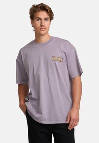 Light purple short-sleeve t-shirt made of cotton with a graphic logo in yellow and pink on the left chest area; loose fit design.