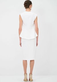 Top peplum bianco aderente con maniche corte abbinato a una gonna al ginocchio. La vista posteriore mette in evidenza una texture liscia e linee pulite.