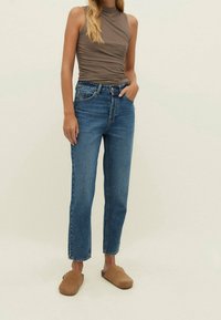 Ljust brunt tajt linne, högmidjade blå jeans och bruna slip-on skor. Jeansen har rak skärning och en diskret blekt tvätt.