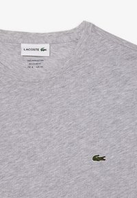 Grå t-shirt med kort ärm gjord av 100% Pima-bomull. Har en liten broderad grön Lacoste-logga på vänster bröst. Regular fit.