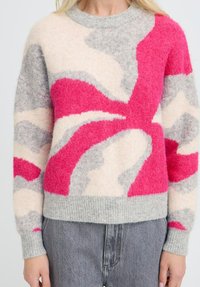 Wollpullover mit abstrakten Farbblöcken in Rosa, Grau und Creme, Rundhalsausschnitt und gerippten Bündchen, getragen mit grauen Denim-Jeans.
