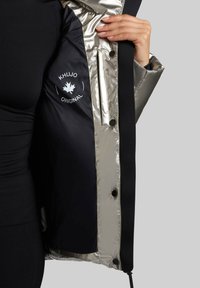 Padded jacket z błyszczącym srebrnym wnętrzem, czarną warstwą zewnętrzną i zapięciem na guziki. Posiada logo na podszewce, gładką teksturę.