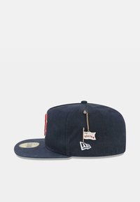 Gorra de béisbol en azul marino con visera plana, logo bordado, un acento rojo y un pequeño detalle de bandera que dice "Campeón Mundial 9 veces Boston".