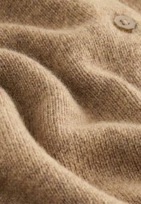 Braun gestrickter Stoff mit einer weichen, strukturierten Oberfläche. Verfügt über einen großen, runden Knopf-Akzent in einer warmen, gedämpften Farbpalette.