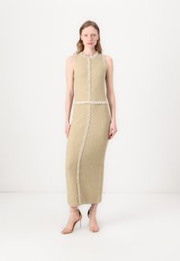 Beige teksturert ermeløs kjole med fuzzy kant langs sømmene og en rett silhuett som når midt på leggen, kombinert med gjennomskinnelige hæler.