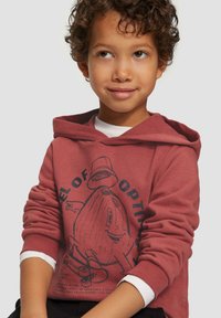 Bordeaux hoodie met een ronde kap, voorzien van een grote afbeelding van een lachend figuur. Witte accentmanchetten op de mouwen, zachte stoftextuur.