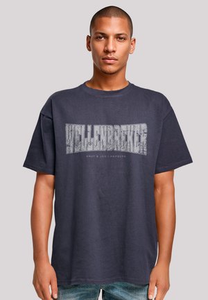Dark grey oversized cotton t-shirt featuring a bold, distressed white "Wellenbreker" graphic on the front. Short sleeves and crew neck.