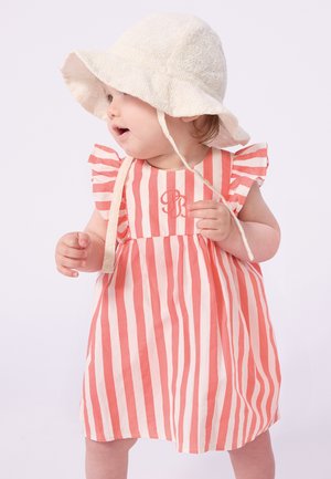 Robe en coton rayée corail et crème avec manches volantées et monogramme brodé. Portée avec un chapeau seau texturé crème.