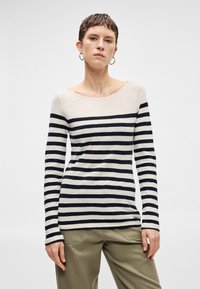 Top de manga longa riscado em bege e azul-marinho, com decote barco e tecido suave. Combinado com calças verdes claras, modelo está de pé contra um fundo neutro.