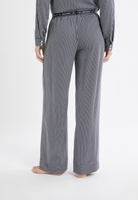 Granatowo-białe paskowane spodnie do piżamy o luźnym kroju, elastyczny pas z napisem "DOG LOVER" oraz mankiety zapinane na guziki. Gładka bawełniana tkanina.