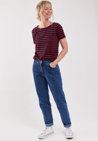 Rood en marineblauw gestreepte t-shirt met korte mouwen, gecombineerd met hoge taille blauwe jeans en witte sneakers. De outfit heeft een losse pasvorm.